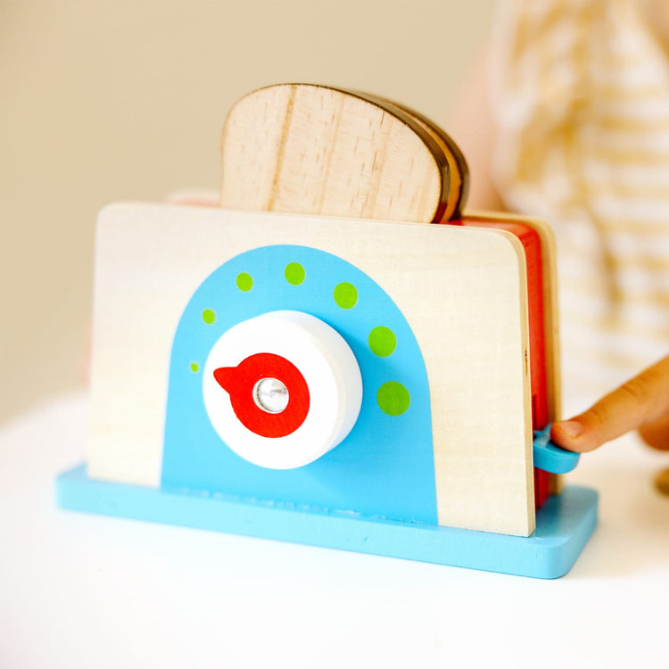 A kid playing with the Melissa & Doug Bread and Butter Toaster Set (9 pcs) - Wooden Play Food and Kitchen Accessories