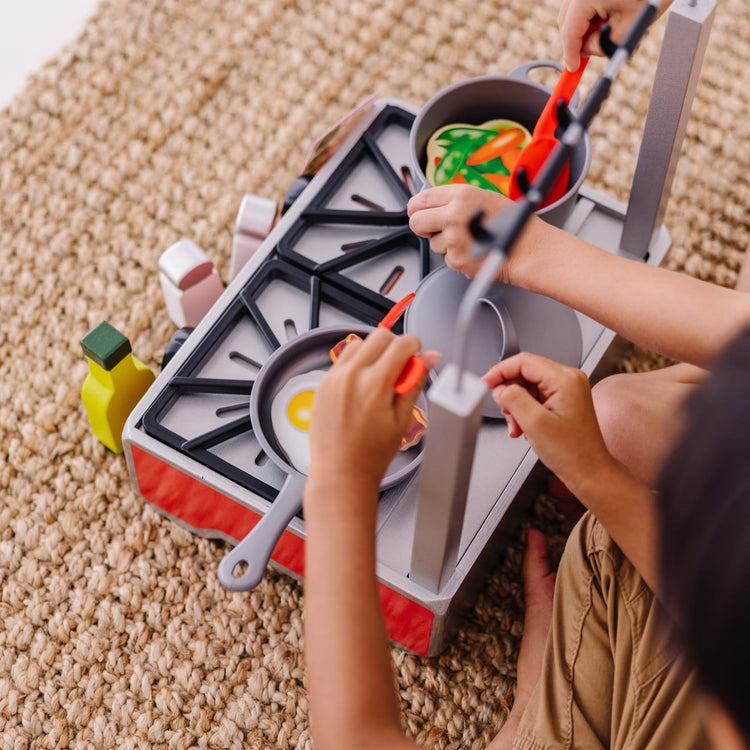 A kid playing with the Melissa & Doug 19-Piece Deluxe Wooden Cooktop Set With Wooden Play Food, Durable Pot and Pan