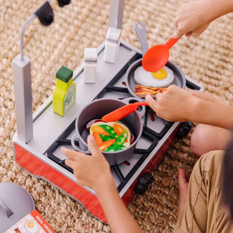 A kid playing with the Melissa & Doug 19-Piece Deluxe Wooden Cooktop Set With Wooden Play Food, Durable Pot and Pan