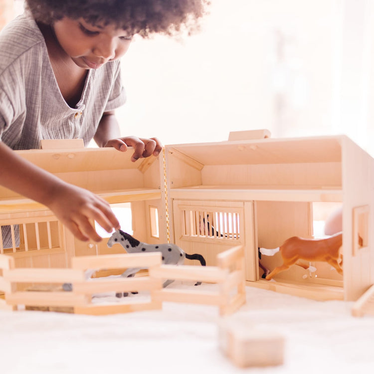 A kid playing with the Melissa & Doug Fold and Go Wooden Horse Stable Dollhouse With Handle and Toy Horses (11 pcs)