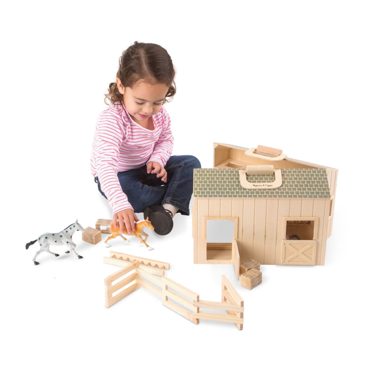 A child on white background with the Melissa & Doug Fold and Go Wooden Horse Stable Dollhouse With Handle and Toy Horses (11 pcs)