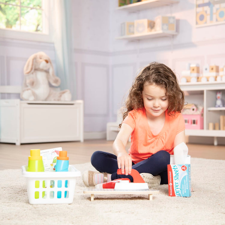 A kid playing with the Melissa & Doug Laundry Basket Play Set With Wooden Iron, Ironing Board, and Accessories (14 Pcs)