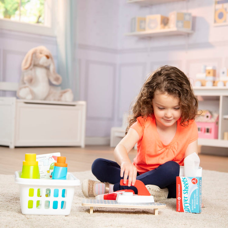 A kid playing with the Melissa & Doug Laundry Basket Play Set With Wooden Iron, Ironing Board, and Accessories (14 Pcs)