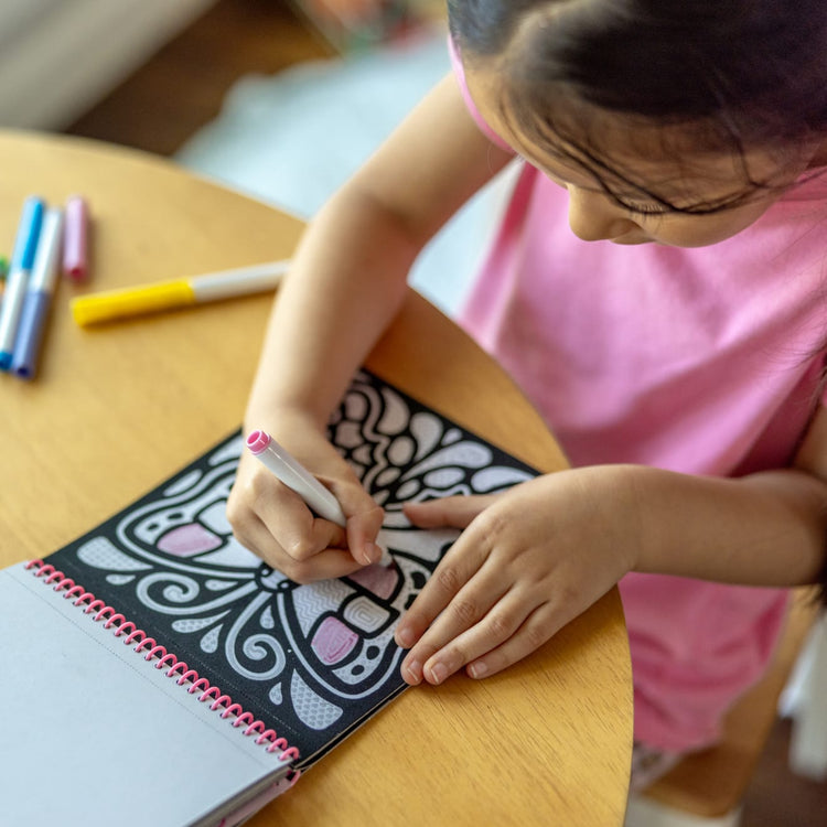 A kid playing with the Melissa & Doug On the Go Magic Velvet Pattern-Reveal Scenes Activity Kit - 6 Coloring Boards, 6 Markers