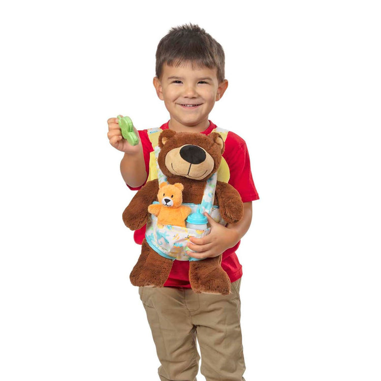 A child on white background with the Melissa & Doug Mine to Love Carrier Play Set for Baby Dolls with Toy Bear, Bottle, Rattle, Activity Card