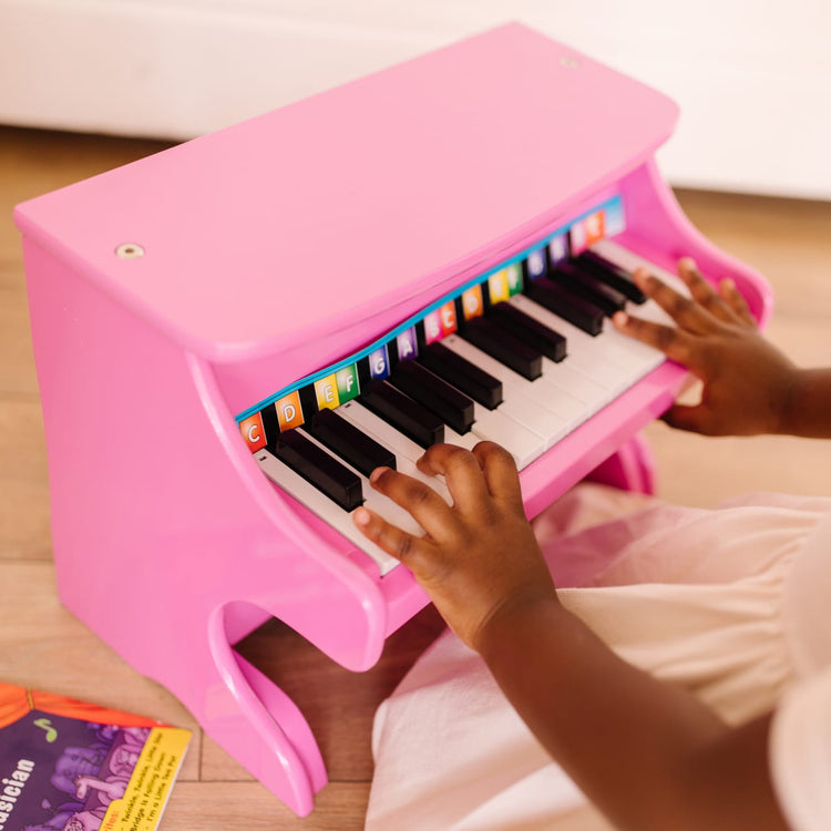 A kid playing with the Melissa & Doug Learn-to-Play Pink Piano With 25 Keys and Color-Coded Songbook