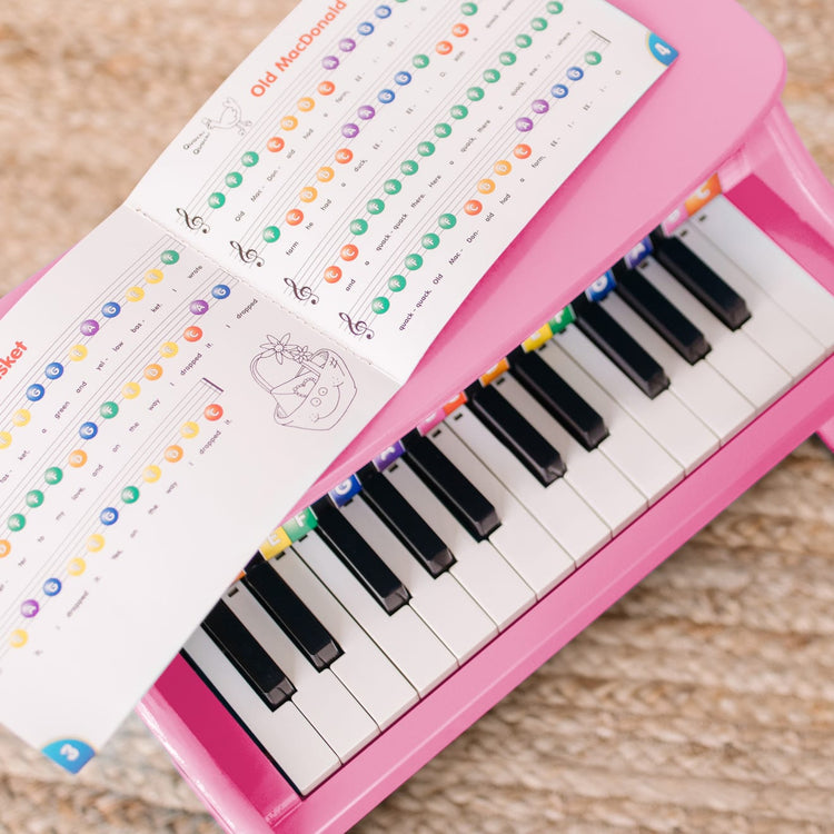 A kid playing with the Melissa & Doug Learn-to-Play Pink Piano With 25 Keys and Color-Coded Songbook