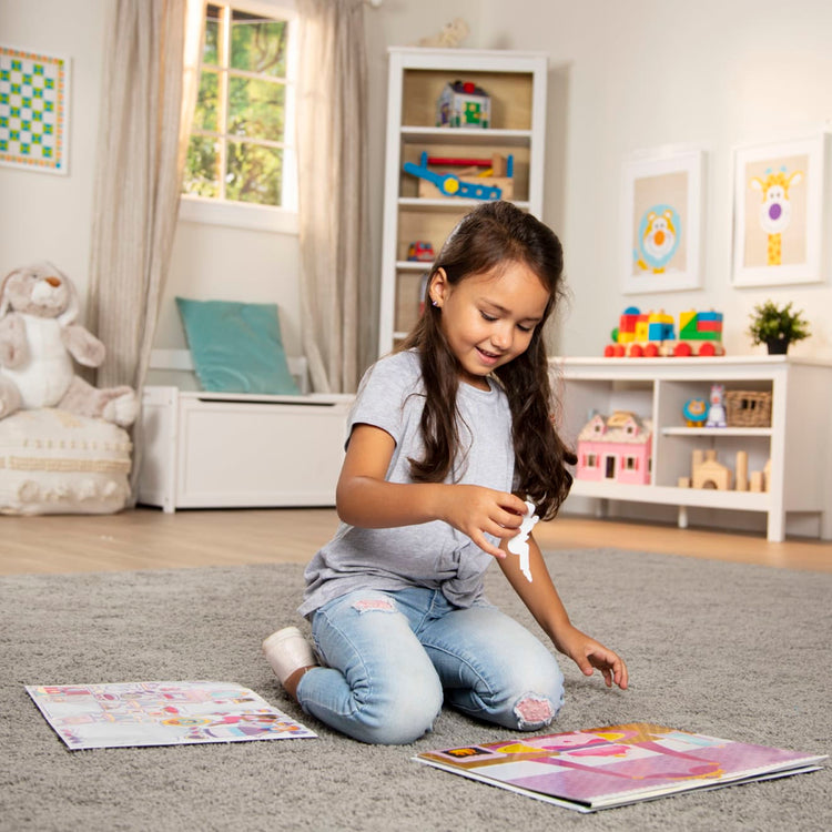 A kid playing with the Melissa & Doug Reusable Sticker Pads Set: Fairies, Princess Castle, Play House, Dress-Up - 680+ Stickers