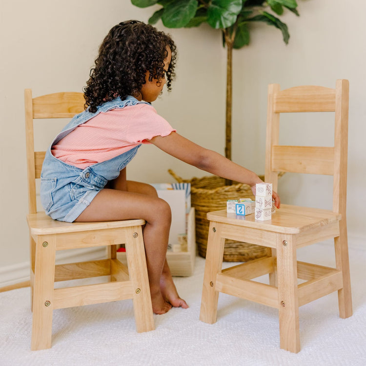 A kid playing with the Melissa & Doug Solid Wood Chairs, Set of 2 - Light Finish Furniture for Playroom