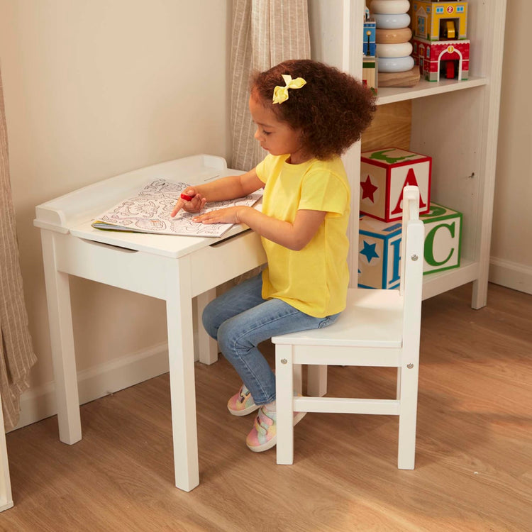 A kid playing with the Melissa & Doug Wooden Child's Lift-Top Desk & Chair - White